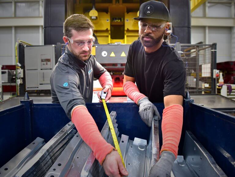 Two men measuring metal with tape measure