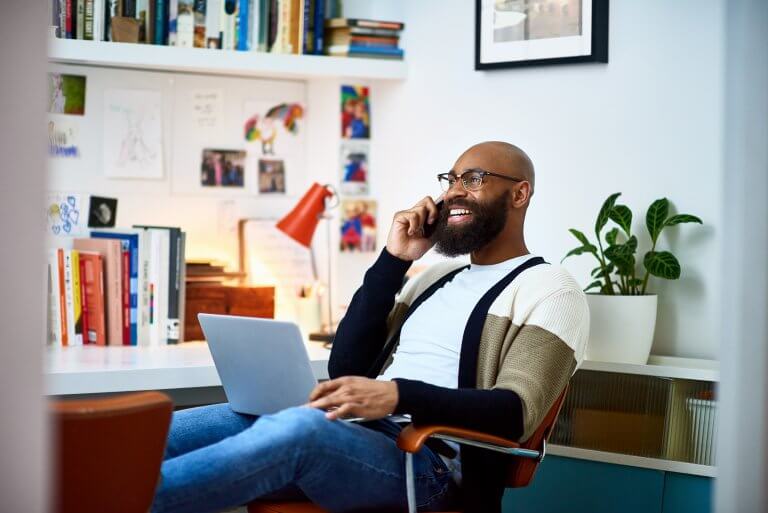 Man speaking on phone with laptop on lap