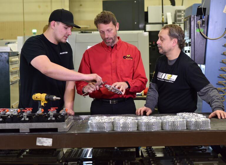 Three men looking at a gear