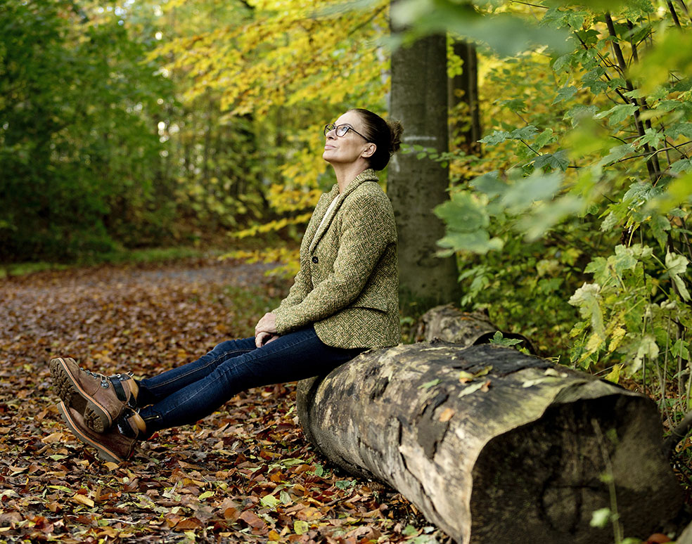 Woman sitting on a tree trunk looking at fall leaves