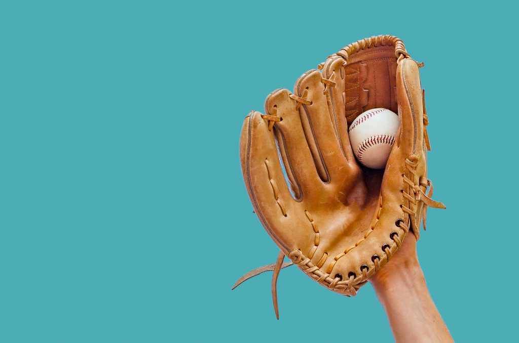 Hand In A Leather Baseball Glove Catches A Baseball on a Blue Background